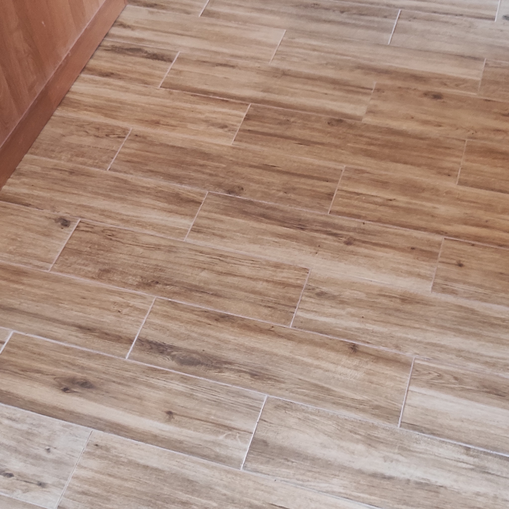 Ukończona podłoga z płytek imitujących drewno, ułożonych w cegiełkę, z widoczną listwą przypodłogową. Jasne fugi podkreślają wzór.