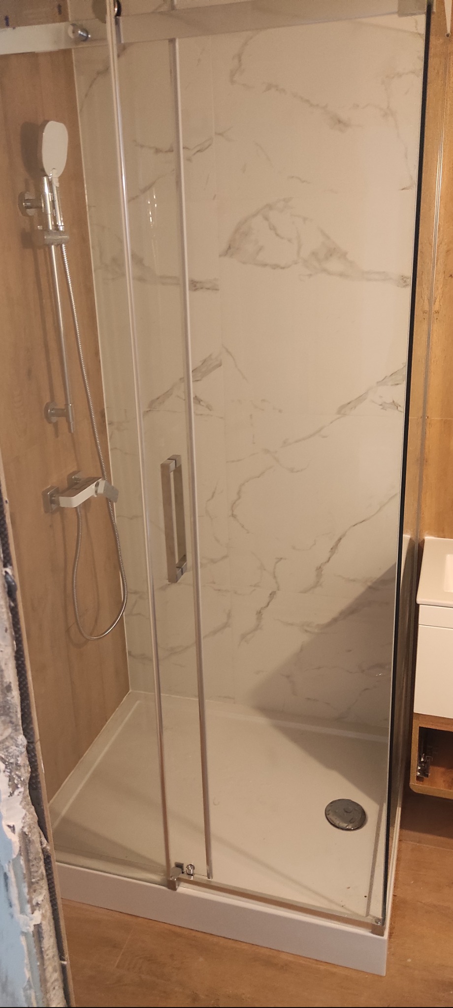 Kabina prysznicowa z marmurowym wzorem na ścianach, chromowaną armaturą i szklanymi drzwiami przesuwnymi, stanowiąca element wykończenia łazienki.