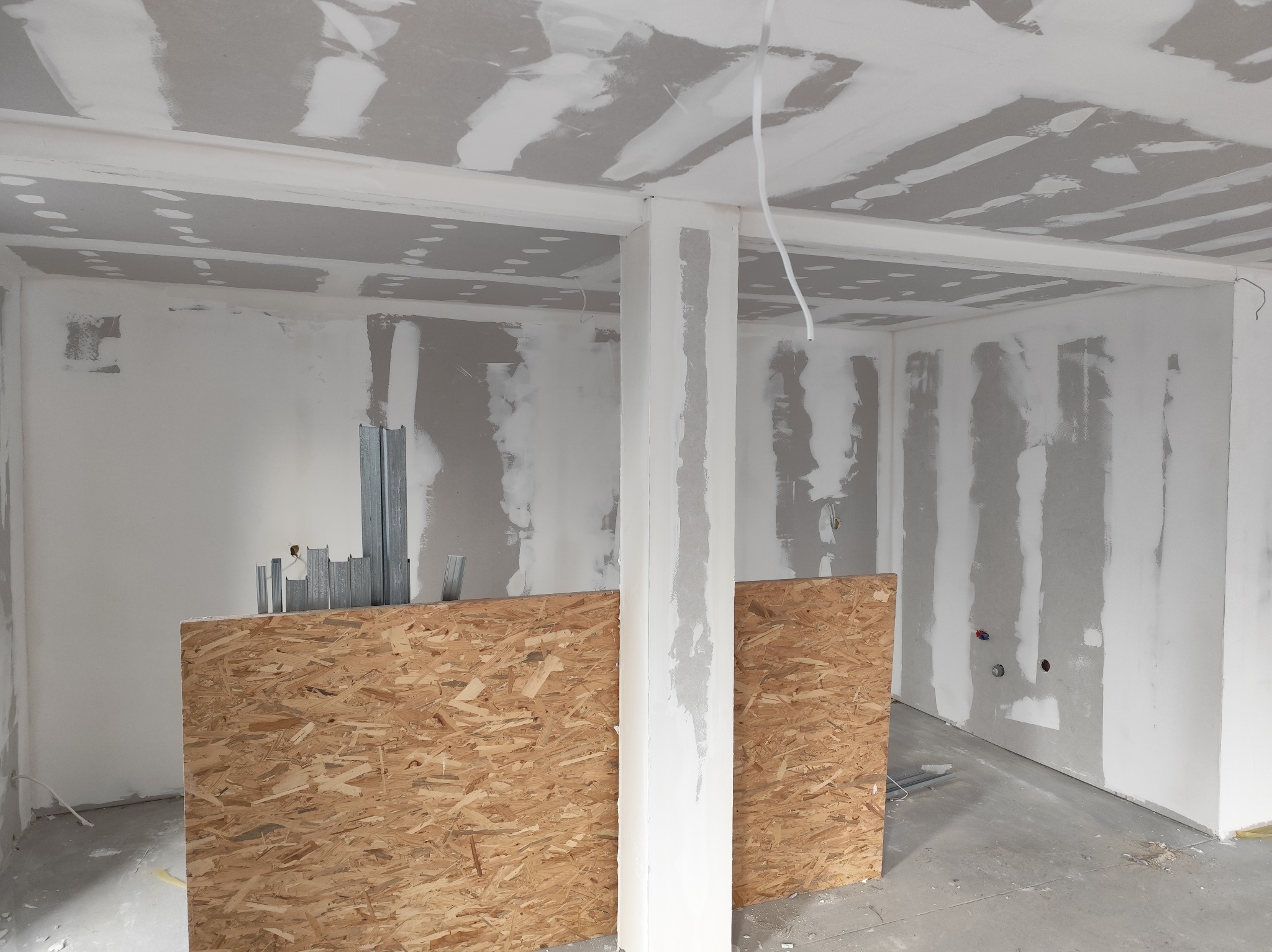Wnętrze w trakcie prac wykończeniowych: ściany z płyt gipsowo-kartonowych, częściowo wyszpachlowane, widoczne profile metalowe i płyta OSB.