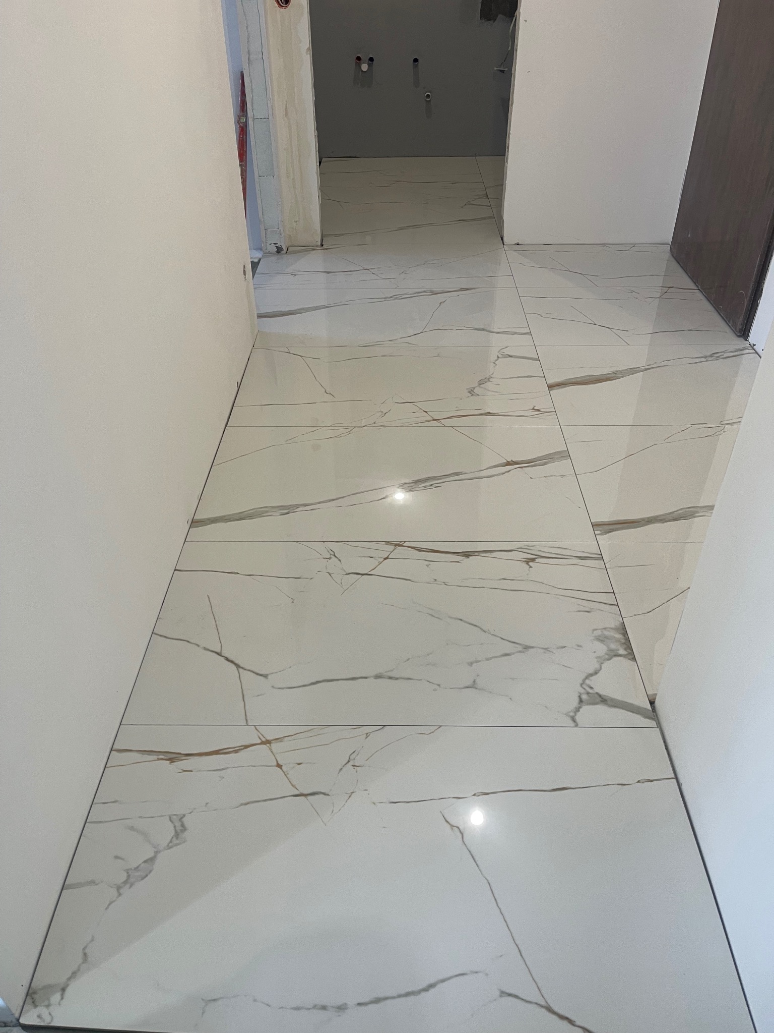 Białe płytki podłogowe z marmurkowym wzorem w korytarzu podczas remontu. Widoczne ściany i futryny drzwiowe w surowym stanie. Minimalistyczny styl wykończenia.