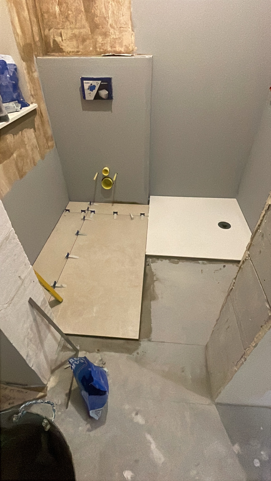 Montaż płytek podłogowych w łazience ze stelażem podtynkowym WC. Użyto poziomicy i krzyżyków dystansowych. Widoczne narzędzia i częściowo położone płytki.