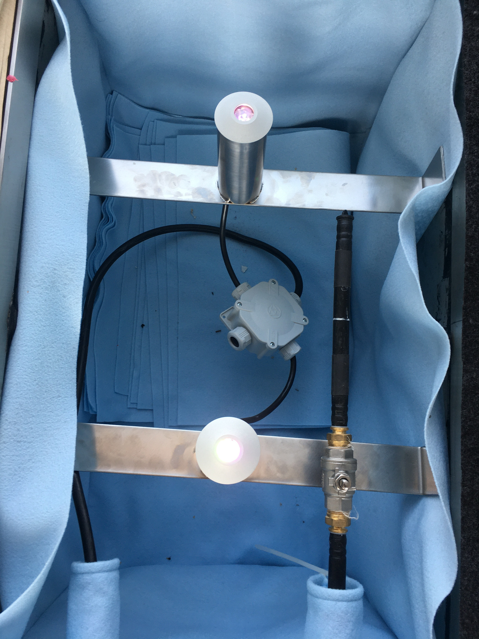 Instalacja oświetleniowa LED w obudowie z niebieskim materiałem, widoczne przewody, puszka elektryczna i zawór, tworzące unikalny układ.