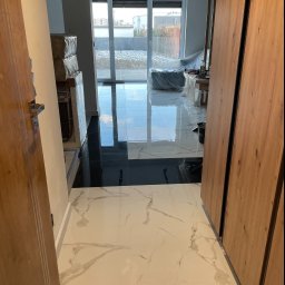 PAWEŁ-BUD Paweł Bulik - Wykończony fragment podłogi z białych i czarnych płytek w nowoczesnym wnętrzu. Widoczne drzwi z drewnianymi okładzinami i okno balkonowe z widokiem na zewnątrz.