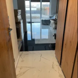 Wykończony fragment podłogi z białych i czarnych płytek w nowoczesnym wnętrzu. Widoczne drzwi z drewnianymi okładzinami i okno balkonowe z widokiem na zewnątrz.