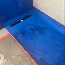 Hydroizolacja w kolorze kobaltowym, z odpływem liniowym w kabinie prysznicowej. Prace w trakcie realizacji w Środzie Wielkopolskiej. Widoczne płytki na ścianie.