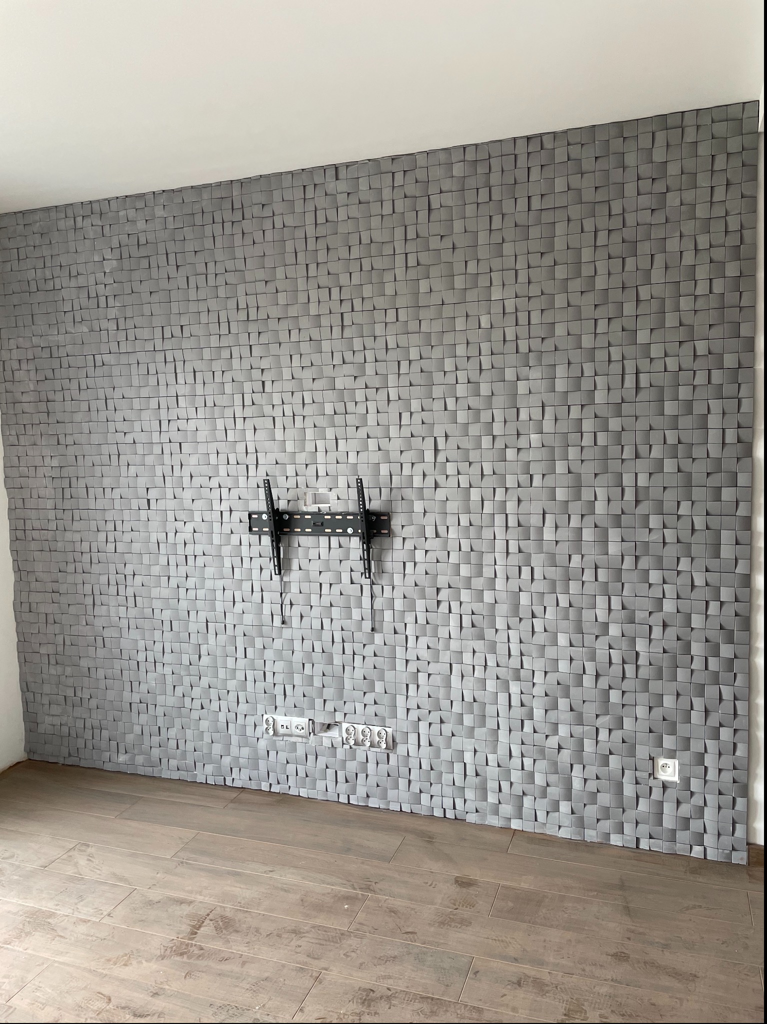 Panel ścienny 3D z szarych kwadratów, uchwyt TV, gniazdka elektryczne i podłoga z paneli. Dekoracyjne wykończenie ściany w nowoczesnym wnętrzu.