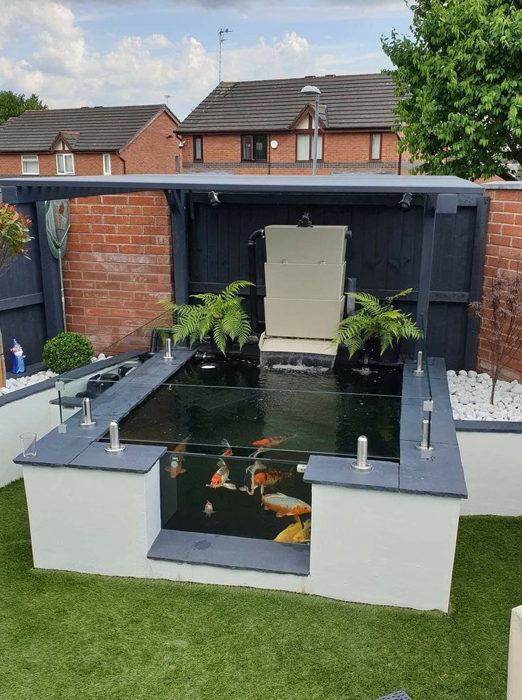 Nowoczesny oczko wodne z przeszkloną ścianą boczną, umożliwiającą obserwację kolorowych ryb koi. Dekoracyjne kamienie, rośliny i oświetlenie podkreślają estetykę.