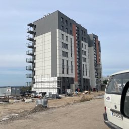 Zakład Budowlany ''Kocięda'' Stefan Kocięda - Wielopiętrowy budynek w trakcie prac elewacyjnych, widoczne rusztowania i ekipa budowlana. Częściowo ocieplona fasada, biała furgonetka z boku kadru.