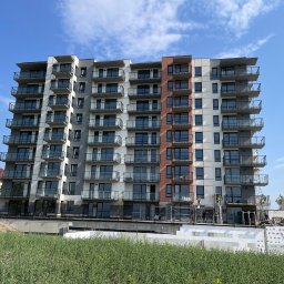 Zakład Budowlany ''Kocięda'' Stefan Kocięda - Wielopiętrowy budynek z balkonami w trakcie prac elewacyjnych. Widoczne rusztowania i pracownicy. Część elewacji szara, część biała z elementami ceglanymi.