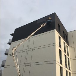 Zakład Budowlany ''Kocięda'' Stefan Kocięda - Malowanie elewacji bloku mieszkalnego z użyciem podnośnika koszowego. Nowoczesna architektura, dwukolorowa fasada. Widoczne numery kontaktowe na ramieniu podnośnika.