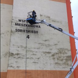Zakład Budowlany ''Kocięda'' Stefan Kocięda - Pracownik na podnośniku czyści elewację budynku z napisem 'Wspólnota Mieszkaniowa Sobieskiego 4'. Widoczne zabrudzenia na ścianie, żółta skrzynka gazowa.