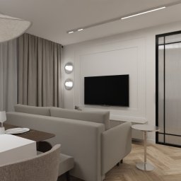 Preludium Design Patrycja Gawryszewska - Jasne wnętrze salonu z jadalnią: beżowa sofa, stół z nakryciem, telewizor na ścianie, dekoracyjne lampy i parkiet w jodełkę. Minimalistyczny design.