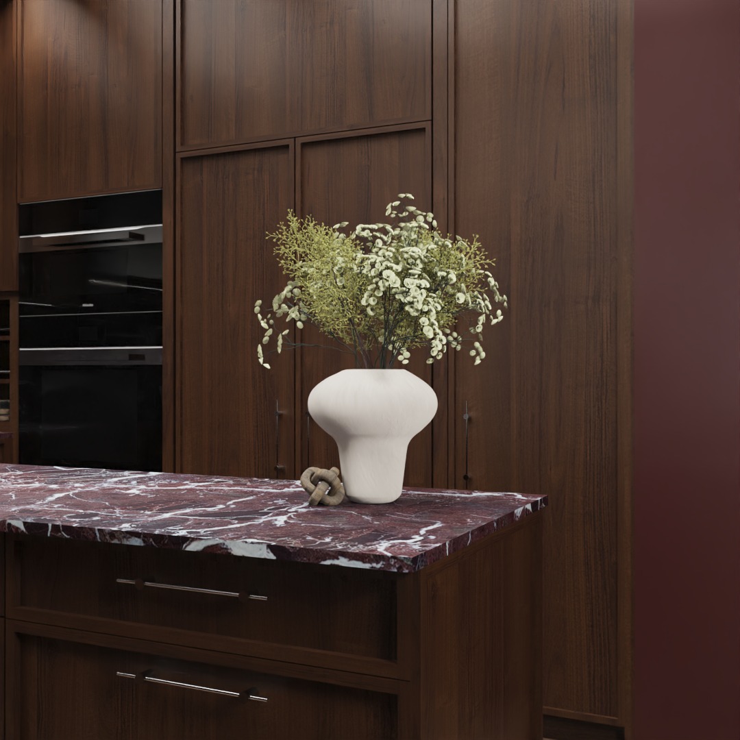 Kuchenna wyspa z blatem z czerwonego marmuru, na której stoi biały wazon z kwiatami. W tle zabudowa meblowa z ciemnego drewna i piekarnik.