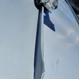 Montaż srebrnej listwy elewacyjnej za pomocą specjalistycznego narzędzia na tle błękitnego nieba. Detal pracy przy elewacji.