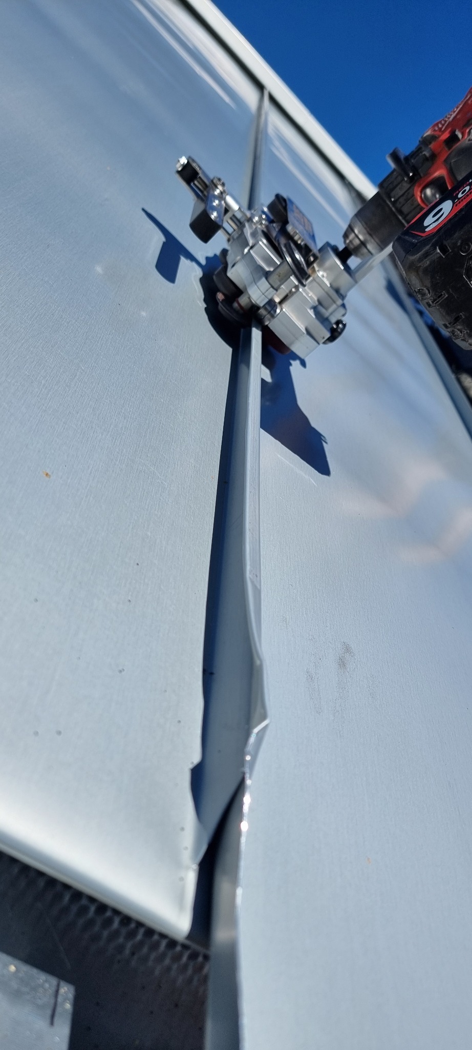 Montaż srebrnej listwy elewacyjnej za pomocą specjalistycznego narzędzia na tle błękitnego nieba. Detal pracy przy elewacji.