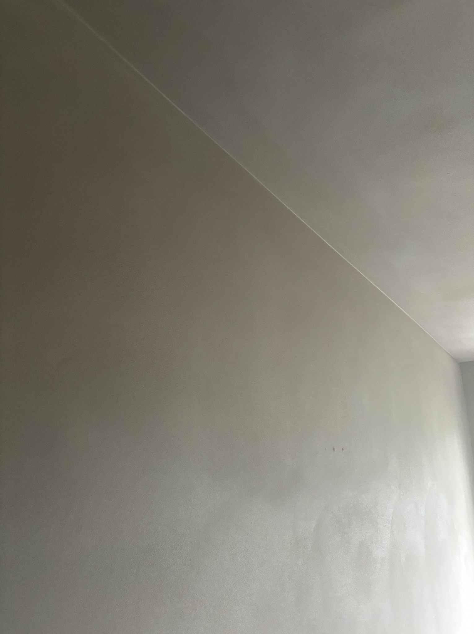 Gładka, szara ściana po nałożeniu tynku maszynowego, widoczne delikatne cieniowanie i linia styku ściany z sufitem. Minimalistyczne ujęcie.