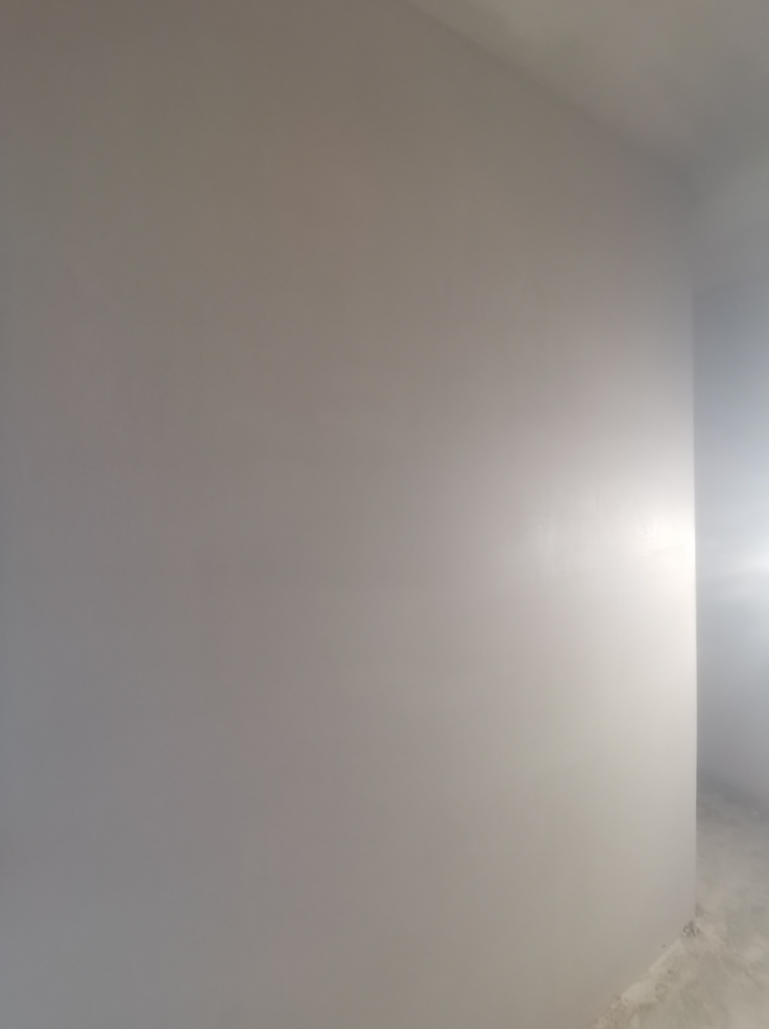 Gładka, szara ściana po nałożeniu tynków w Obidowej. Minimalistyczne wykończenie wnętrza, widoczny narożnik ściany i fragment podłogi.