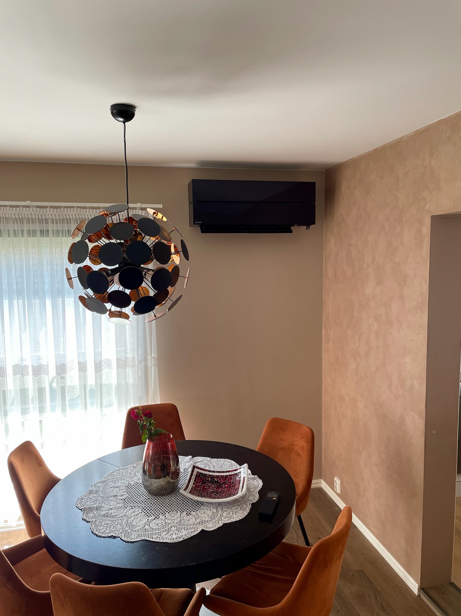 Nowoczesny klimatyzator ścienny w eleganckim salonie z okrągłym stołem i designerską lampą. Minimalistyczny design w stonowanych kolorach.