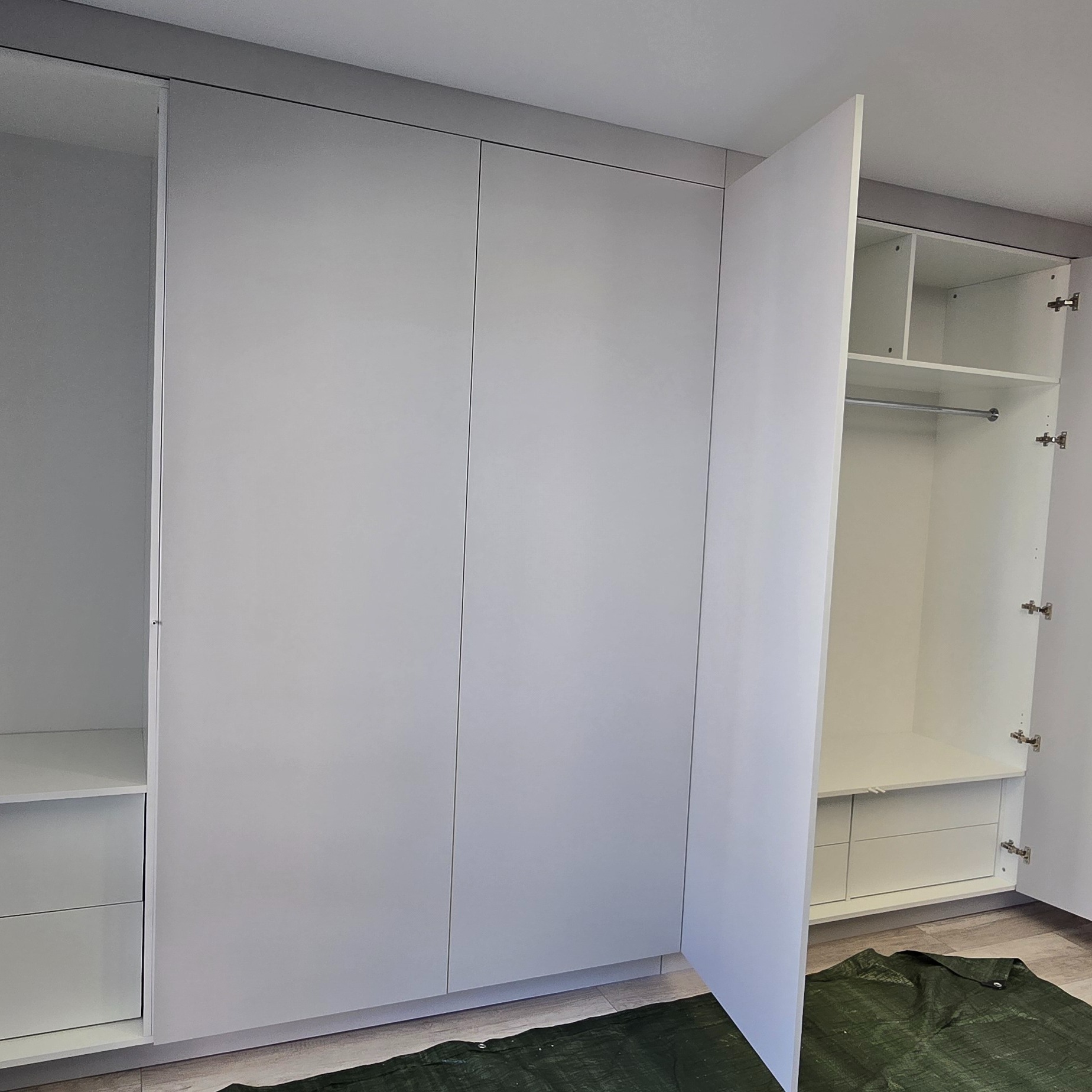 Nowoczesna, biała szafa na wymiar z otwartymi drzwiami, ukazująca półki i drążek na ubrania. Minimalistyczny design, widoczne okucia.