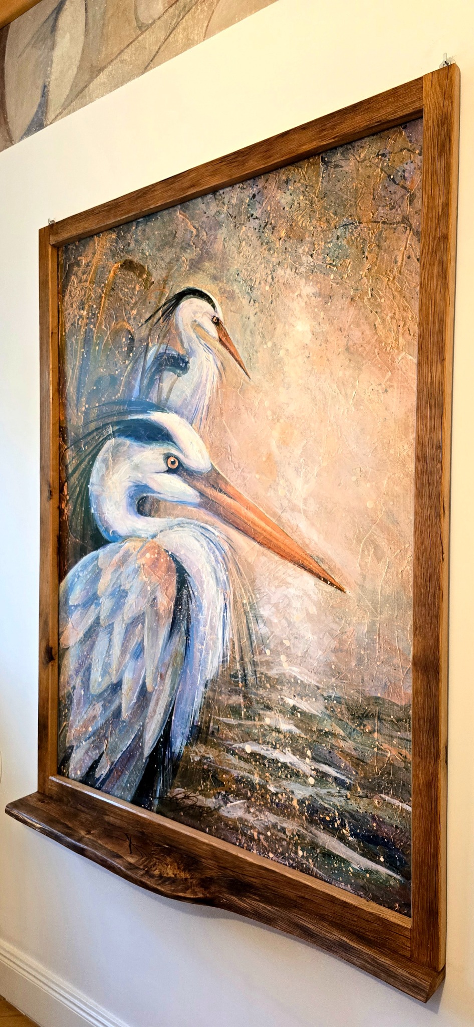 Obraz z motywem dwóch czapli w drewnianej ramie z półką, wiszący na ścianie. Widoczne detale faktury farby i naturalne wykończenie drewna ramy.