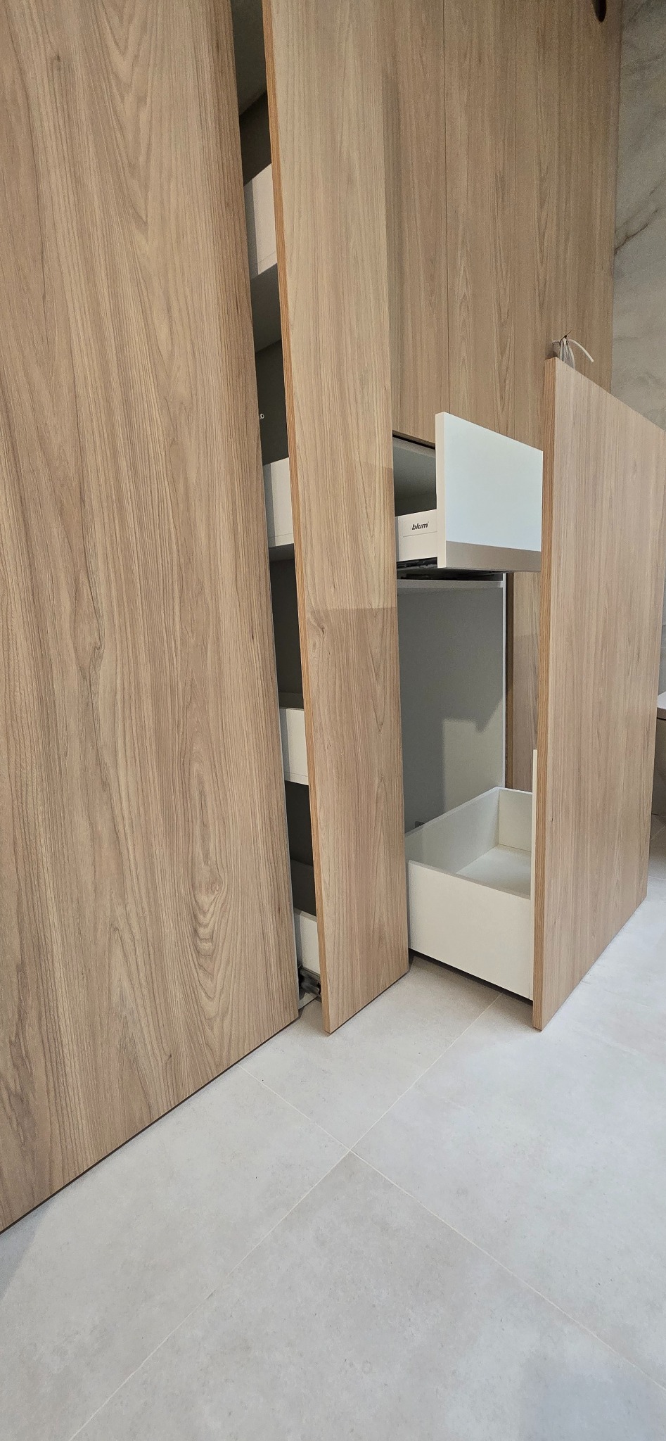 Drewniana szafa z wysuwanymi szufladami w Gdyni. Jasne fronty, minimalistyczny design. Widoczne detale systemu Blum. Nowoczesne rozwiązanie do przechowywania.