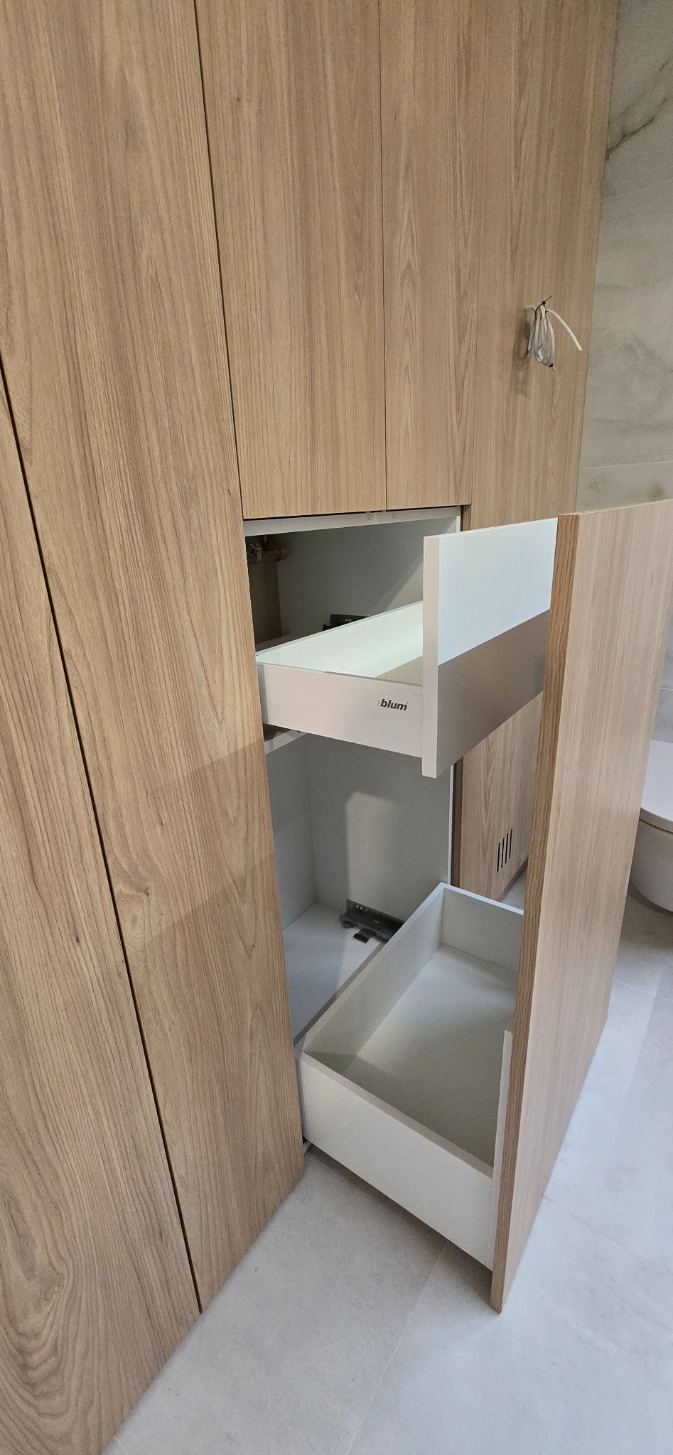 Jasna, drewniana szafa z otwartymi szufladami Blum, ukazująca precyzję wykonania i funkcjonalność. Widoczne detale wykończenia i systemy szuflad.