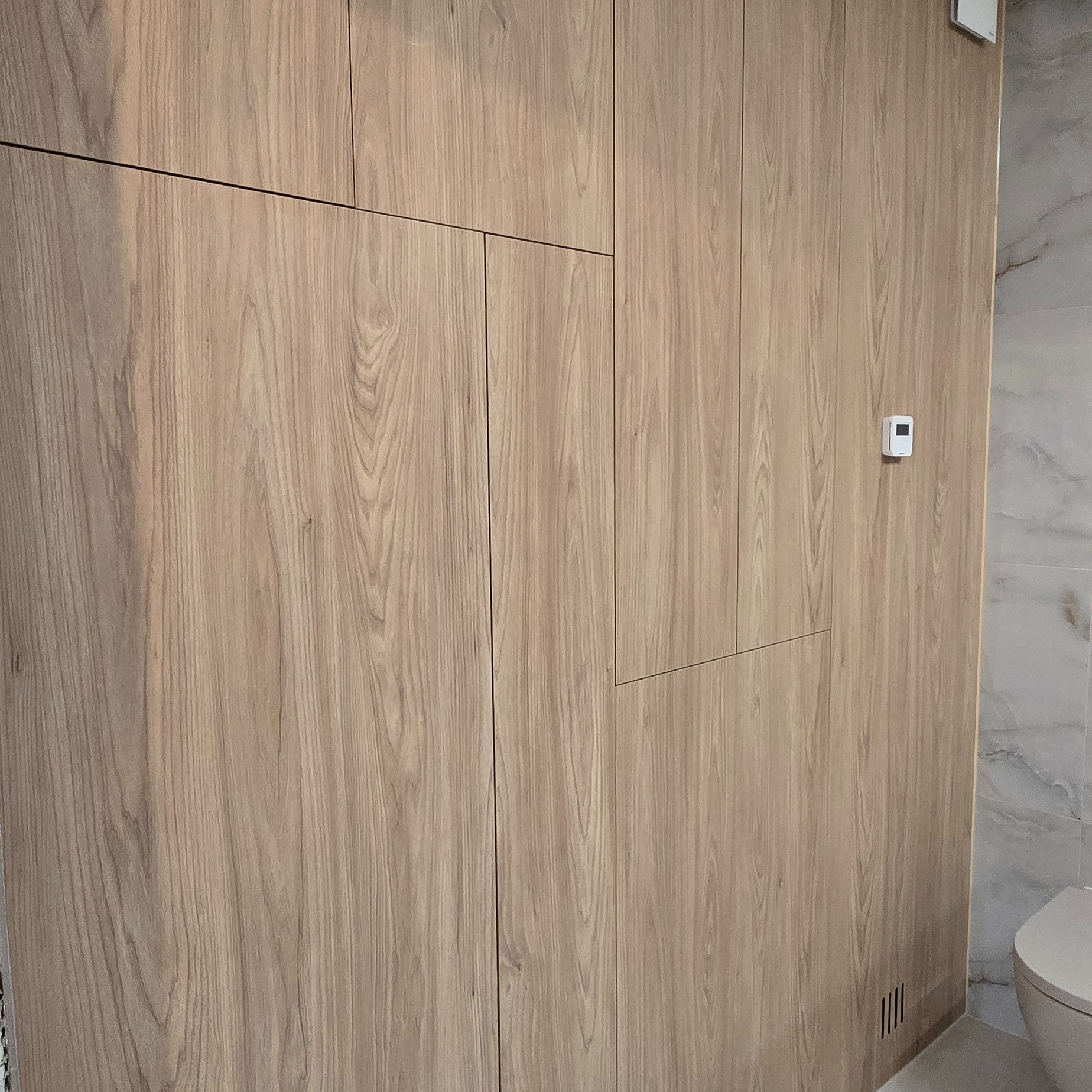 Drewniana zabudowa w łazience z ukrytymi drzwiami i panelem sterowania. Naturalna kolorystyka drewna, minimalistyczny design, widoczne detale wykończenia.