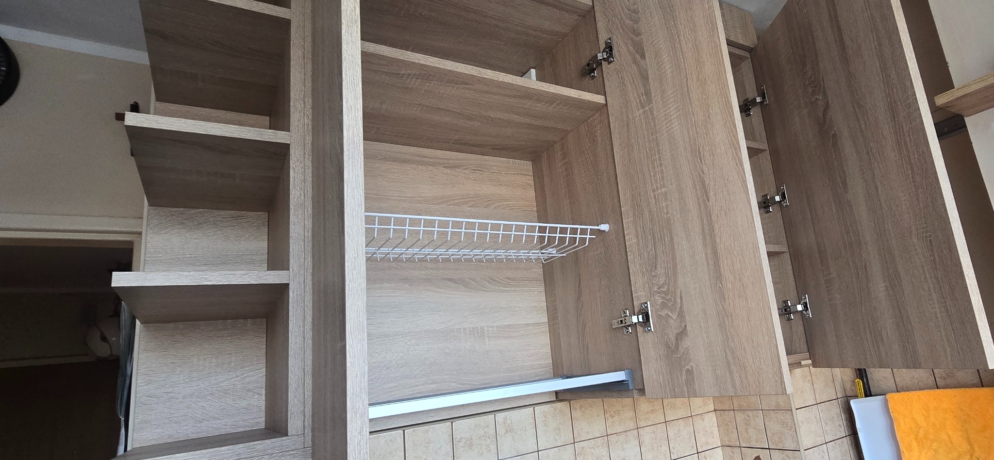 Jasne, drewnopodobne szafki kuchenne z otwartymi drzwiczkami i wysuwaną półką z drutu, ukazujące wnętrze i mechanizmy. Widok z dołu.