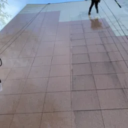 Pracownik alpinistyczny myje elewację budynku z płytek, widoczne różnice czystości. Prace wysokościowe z użyciem sprzętu alpinistycznego i lancy ciśnieniowej.