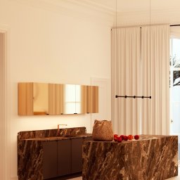 Ewa Stankiewicz EST Interior - Ekskluzywna kuchnia z wyspą wykończoną marmurem, złote szafki wiszące, minimalistyczna lampa sufitowa. Na blacie koszyk i jabłka. Eleganckie wnętrze.