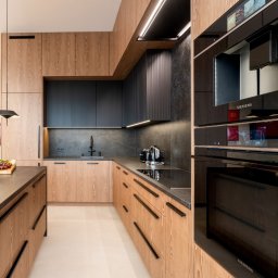 Ewa Stankiewicz EST Interior - Nowoczesna kuchnia na wymiar z drewnianymi frontami i czarnymi akcentami. Widoczne sprzęty AGD marki Siemens, minimalistyczne oświetlenie i kamienny blat.