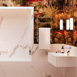 Ewa Stankiewicz EST Interior - Nowoczesna łazienka z wanną obudowaną marmurem, umywalką z szafką i grzejnikiem na ręczniki na tle ściany z wzorzystą tapetą. Brązowo-biała podłoga.