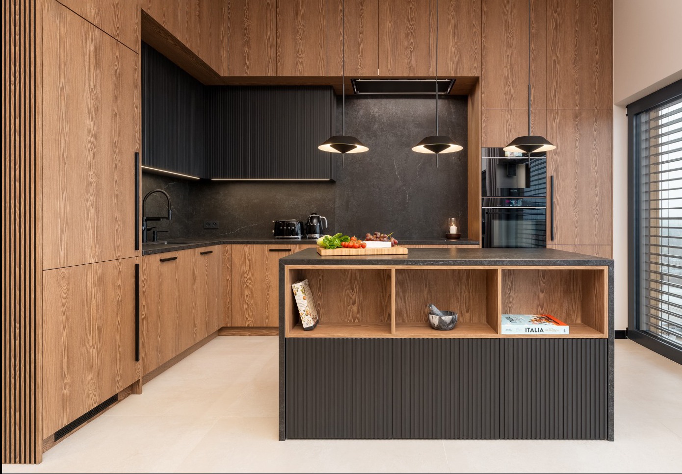Nowoczesna kuchnia z drewnianymi frontami i czarnym blatem. Wyspa kuchenna z otwartymi półkami. Minimalistyczne lampy wiszące. Duże okno z żaluzjami.