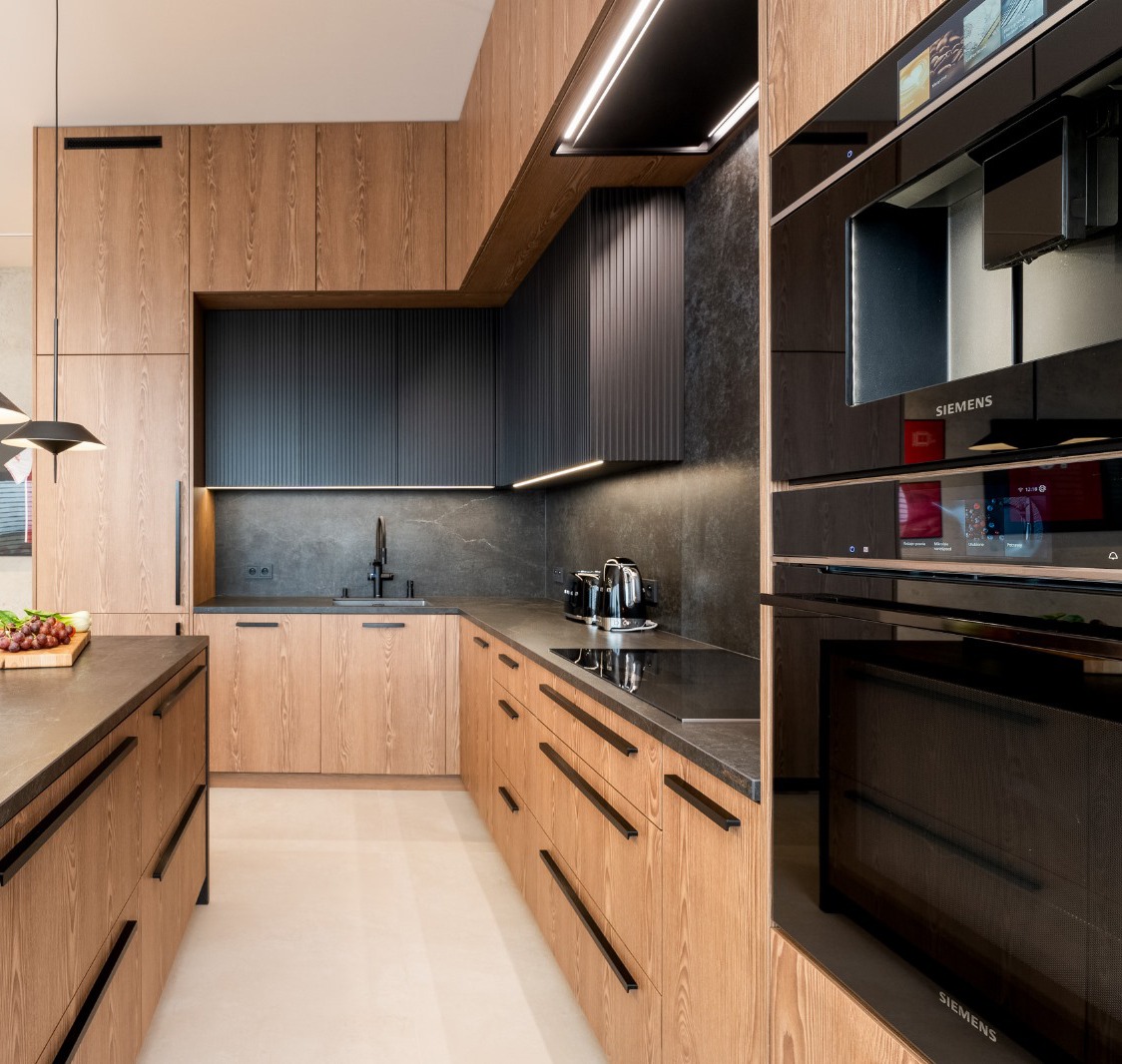 Nowoczesna kuchnia na wymiar z drewnianymi frontami i czarnymi akcentami. Widoczne sprzęty AGD marki Siemens, minimalistyczne oświetlenie i kamienny blat.