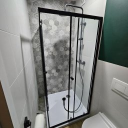 Invest-Bud - Kabina prysznicowa z czarnymi profilami i deszczownicą, w wykończonej łazience w Toruniu. Na ścianie płytki w geometryczne wzory.