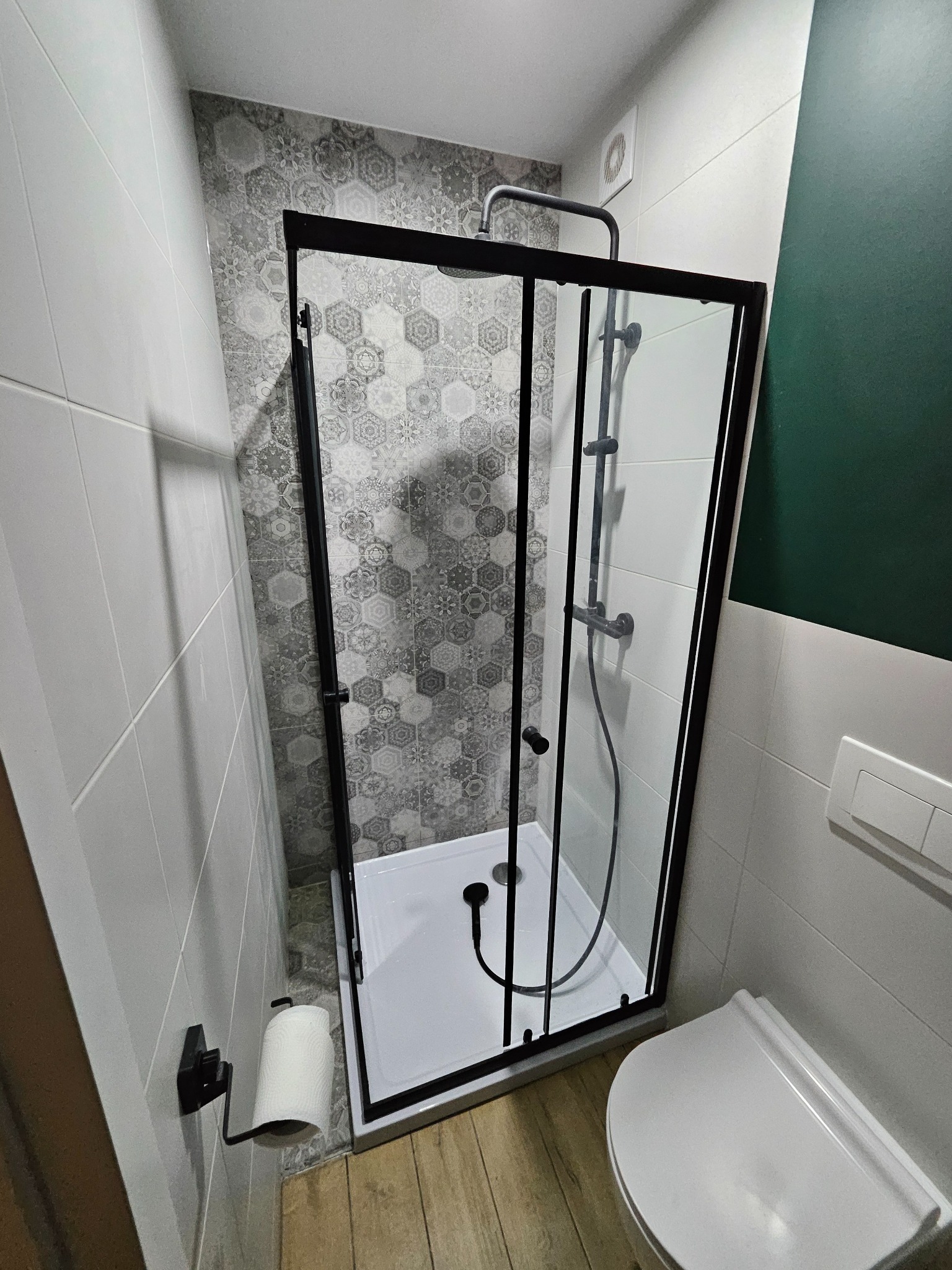 Kabina prysznicowa z czarnymi profilami i deszczownicą, w wykończonej łazience w Toruniu. Na ścianie płytki w geometryczne wzory.