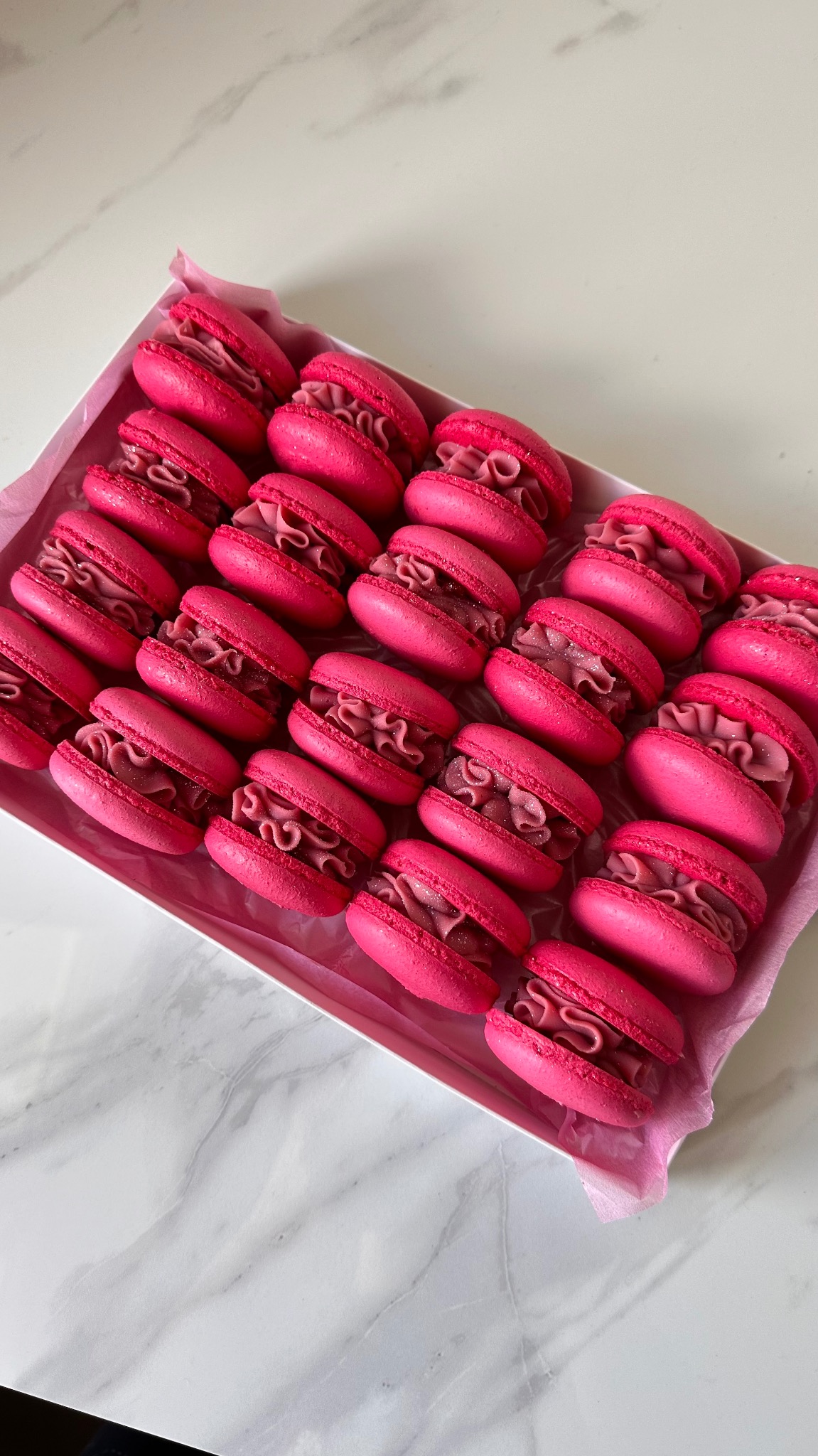 Rząd różowych makaroników z kremem w białym pudełku na marmurowym tle. Widok z góry, ostre światło.