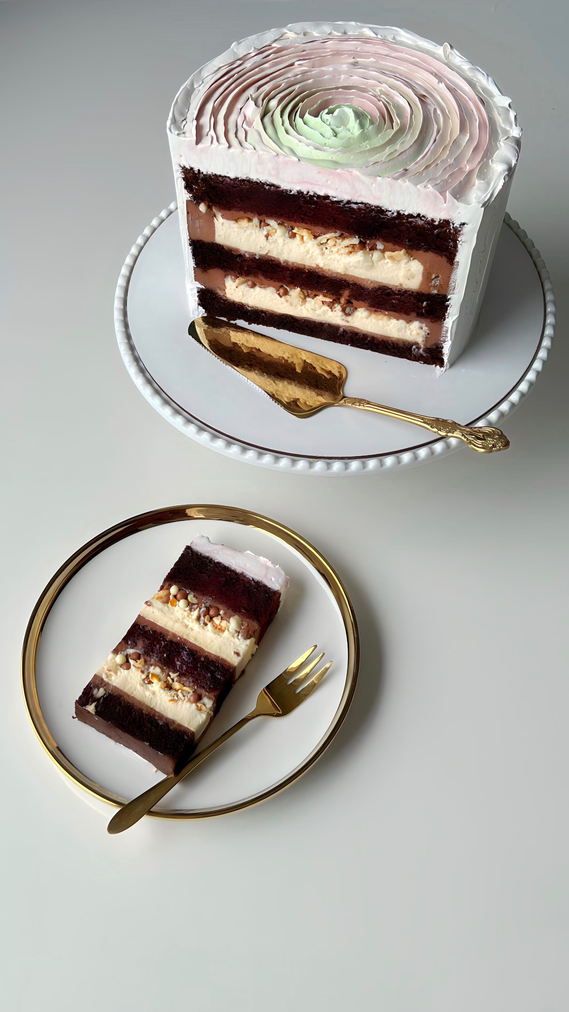 Przekrój tortu z kremem, orzechami i czekoladą na białych talerzach ze złotymi sztućcami. Dekoracja z kremu w odcieniach różu i zieleni. Elegancki deser.