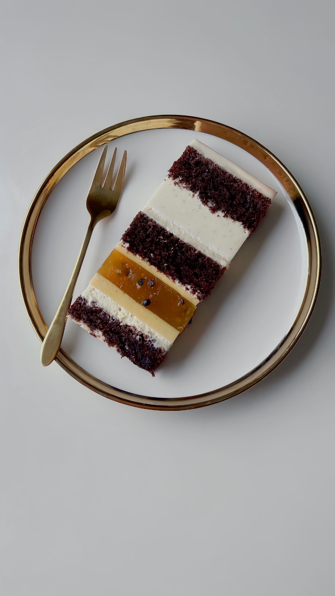 Kawałek tortu z kremem i galaretką z marakui na białym talerzu ze złotym obramowaniem, obok złoty widelec. Eleganckie i apetyczne.