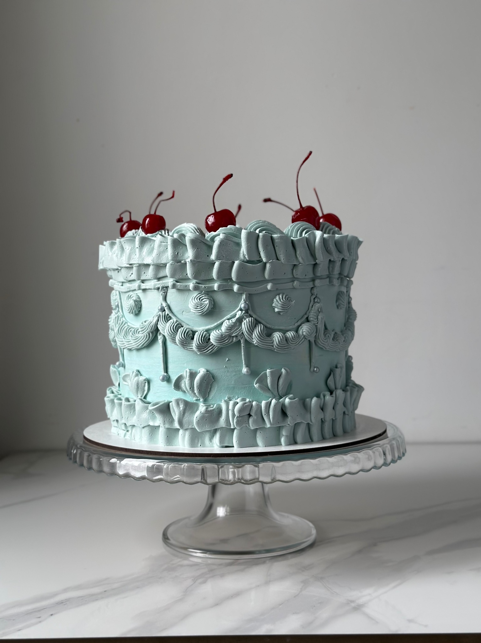 Niebieski tort w stylu retro z wisienkami na paterze, wykonany w cukierni w Sopocie. Dekoracyjny krem i elegancki wygląd.