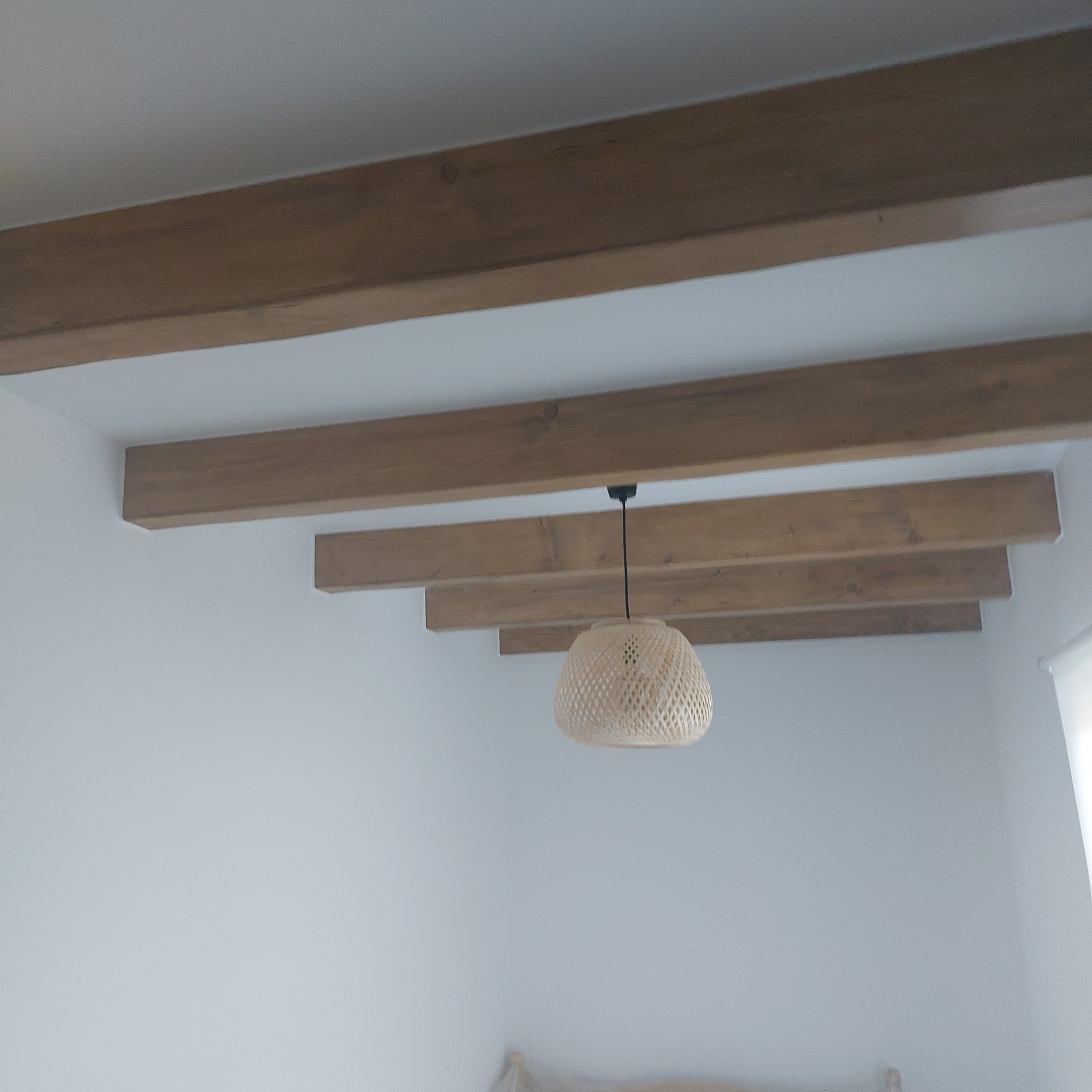 Jasne wnętrze z drewnianymi belkami stropowymi i wiklinową lampą. Widok z dołu na sufit, delikatne oświetlenie.