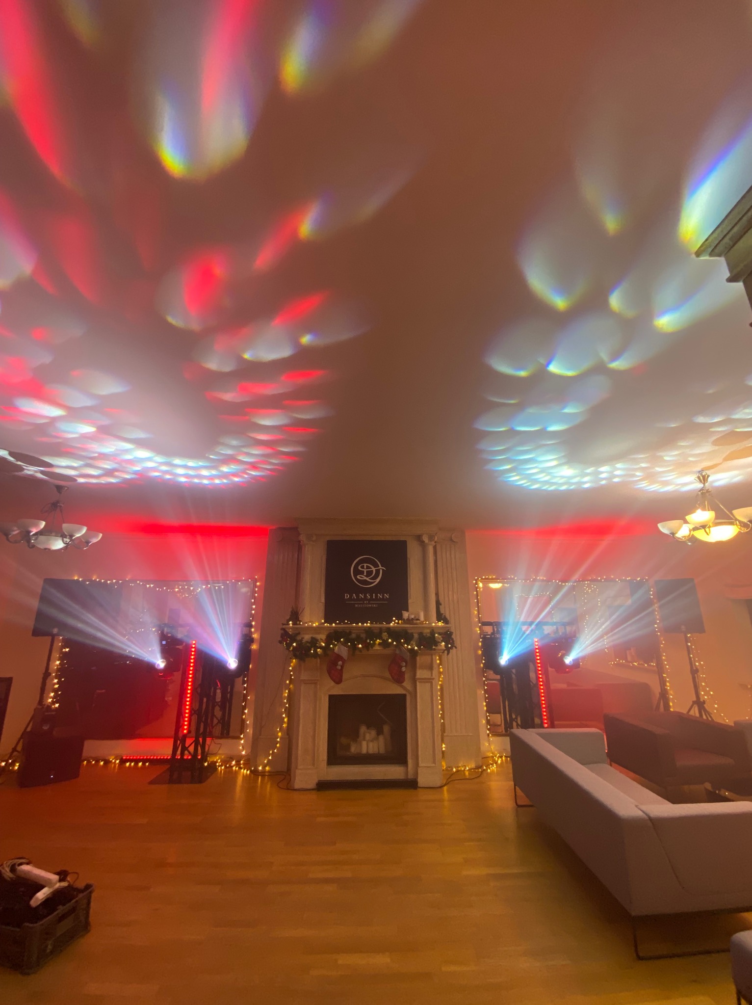 Eleganckie wnętrze z kominkiem, oświetlone dynamicznymi światłami scenicznymi w kolorach czerwieni i błękitu, tworzącymi wzory na suficie. Dekoracje świąteczne.