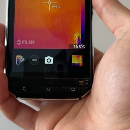 Cleanco Kacper Silecki - Termowizja: telefon FLIR w dłoni, ekran pokazuje rozkład temperatur, 19.4°C w centrum, 16.8°C w rogu. Wykorzystanie termowizji w diagnostyce i inspekcjach.