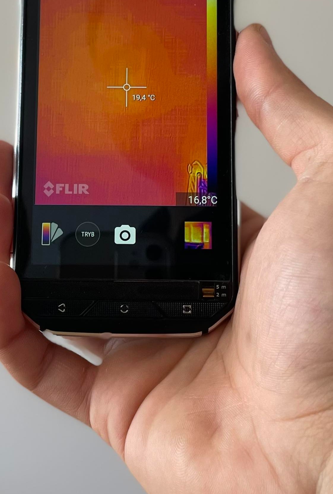 Termowizja: telefon FLIR w dłoni, ekran pokazuje rozkład temperatur, 19.4°C w centrum, 16.8°C w rogu. Wykorzystanie termowizji w diagnostyce i inspekcjach.