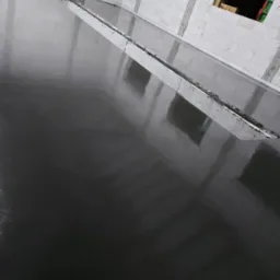 Świeżo wylana, ciemna posadzka przemysłowa, z widoczną listwą dylatacyjną w surowym wnętrzu budynku z białego bloczka.