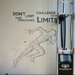 Druk na ścianie w Krapkowicach: grafika biegacza i motywacyjne hasło wykonane za pomocą specjalistycznej drukarki pionowej, widocznej obok. Nowoczesny design.