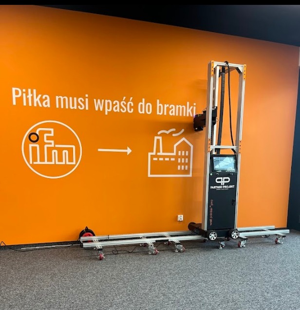 Pomarańczowa ściana z białym napisem i grafiką. Na podłodze stoi drukarka do ścian Wall Printer T Pro. Wyjątkowy sposób na wykończenie wnętrz.