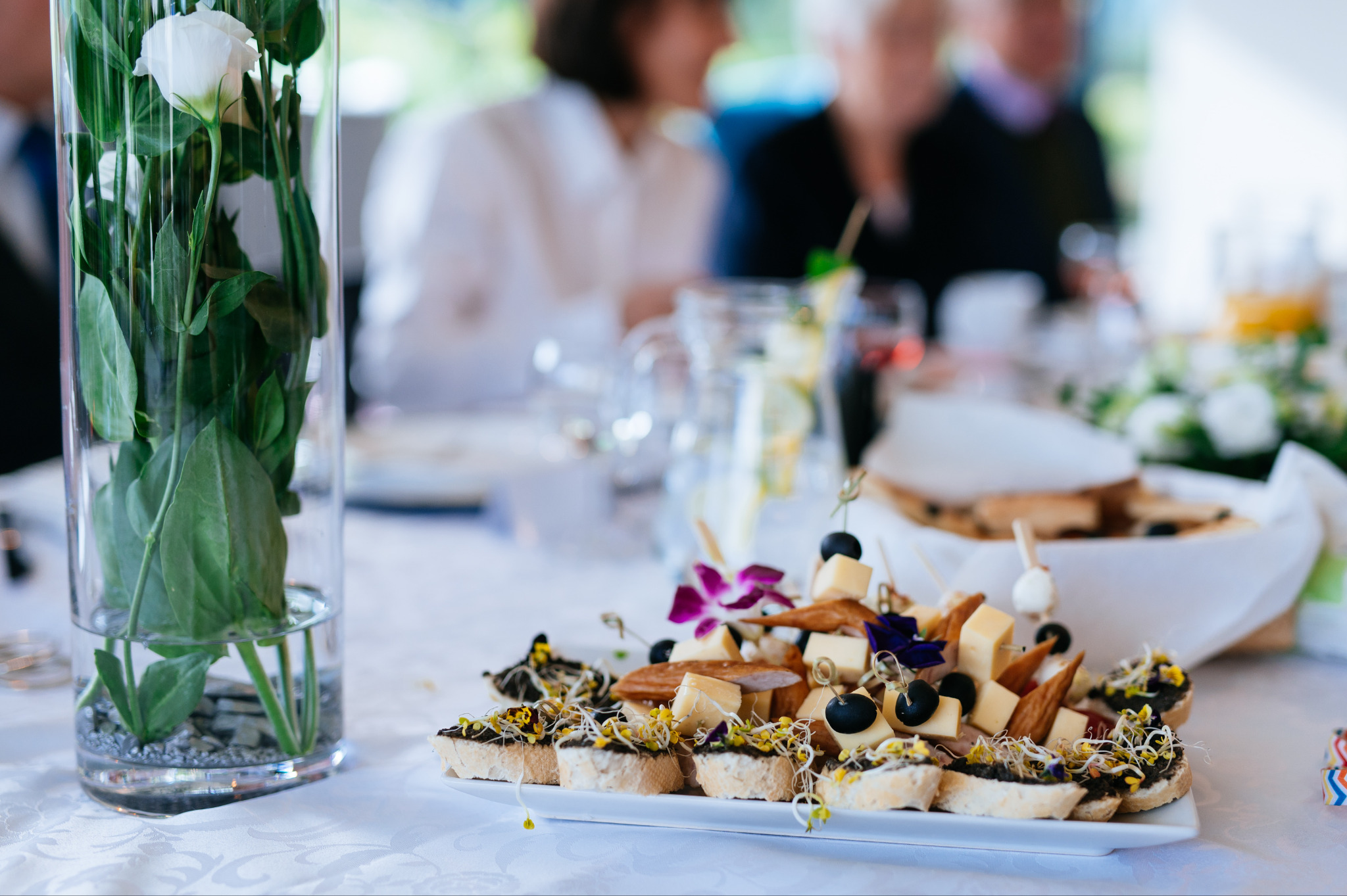 Dekoracyjny stół z przekąskami: kanapeczki z kiełkami, koreczki z serem i oliwkami, wazon z kwiatami. Eleganckie przyjęcie z cateringiem.