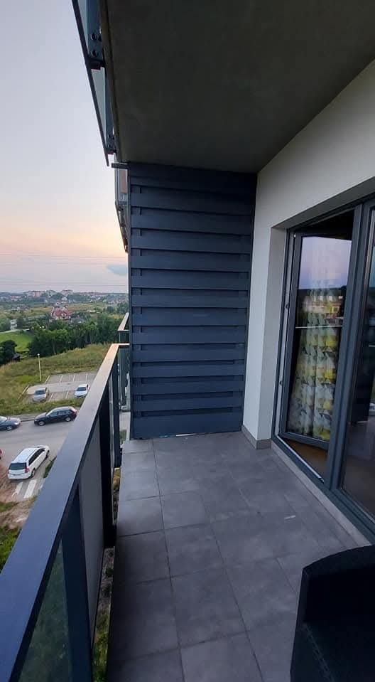 Nowoczesna zabudowa balkonu z szarymi panelami drewnianymi i szklaną balustradą, widok na panoramę miasta o zmierzchu. Eleganckie wykończenie.