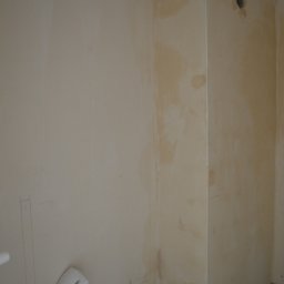 Art Design Grzegorz Kędzierski - Ściana w trakcie przygotowania do malowania z widocznymi śladami po szpachlowaniu i instalacją hydrauliczną u dołu. Widoczny otwór wentylacyjny w rogu.